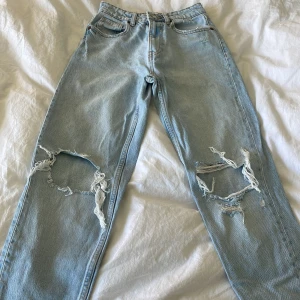 Ljusblå slitna jeans från Zara - Ljusblå jeans från Zara med raka ben och stora slitningar över båda knäna. Klassisk femficksmodell med knapp och dragkedja i gylfen. Perfekta för en avslappnad och trendig look och din blå färg nu till sommaren