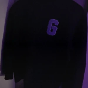 Svart sweatshirt från Glorious Gangsta - Svart sweatshirt med stor vit bokstav 'G' på bröstet och texten 'GLORIOUS' i vitt över ryggen. Klassisk passform och rund hals. Perfekt för en streetwear-look.