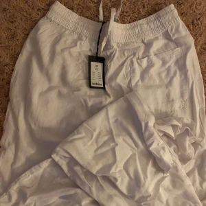 Vita linnebyxor med dragsko - Säljer ett par vita linnebyxor med resår och dragsko i midjan. Byxorna har raka ben och en bakficka. 🥰helt nya!!