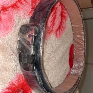  bälte med silverfärgat spänne - Säljer ett bälte med klassiskt damiermönster i svart och grått.  och är tillverkat i skinn. Perfekt accessoar för att lyfta din outfit.