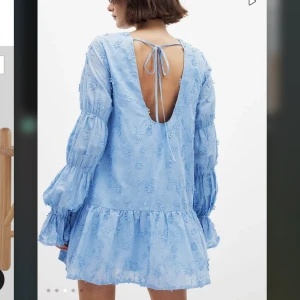 Ljusblå blommig klänning med öppen rygg - Supersöt ljusblå klänning med blommigt mönster och volang nertill. Långa puffärmar med resår och öppen rygg som knyts i nacken. Helt oanvänd med prislapp kvar, säljer då jag köpte två storlekar och glömde att lämna tillbaka i tid!