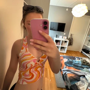 Färgglad swirl mönstrad croppad linnetopp - Säljer en croppad linnetopp med swirl mönster i rosa, orange, gul och vit. Toppen har djup v-ringning och en ringdetalj framtill. Perfekt för sommaren och ger en riktigt retro vibe! Den är aldrig använd (förutom på bilden)