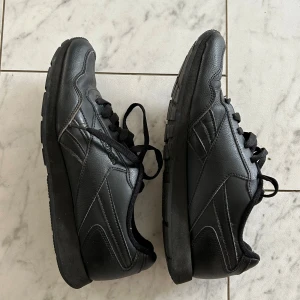 Svarta Reebok sneakers i skinn - Svarta sneakers från Reebok i skinn med klassisk design och svarta snören. Skorna har rund tå och platt sula, perfekt för en stilren look. Reebok-logga på sidan och under sulan. Väldigt bra skick. 