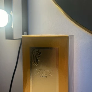 Voux Zeste parfym från Emir - Lyxig parfymflaska i klargul färg med gulddetaljer och elegant lejonmotiv. Flaskan har en exklusiv känsla med metallisk guldkork och präglad etikett framtill. Kommer i matchande guldfärgad förpackning. Doften heter Zeste. Knappt använd