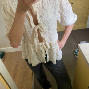 Vit blus med knyt fram - Säljer en vit blus med struktur och tre knyt framtill. Blusen har korta puffärmar och volang nedtill. Perfekt för dig som gillar en luftig och trendig stil.