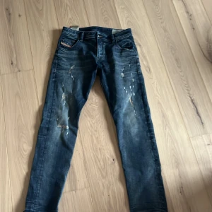 Blå Diesel jeans med slitningar - Säljer ett par blå Diesel Larkee jeans med snygga slitningar och raka ben. Jeansen har klassisk femficksdesign och normal passform. Perfekta för dig som gillar en avslappnad men stilren look. 