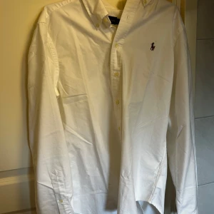 Vit skjorta från Ralph Lauren - Klassisk vit skjorta från Ralph Lauren med broderad logga på bröstet. Perfekt inför sommaren! Nypris ligger på ca 2000, mitt pris 500. Den är i extremt bra skick för så långt pris.