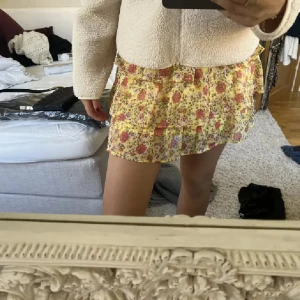 Blommig gul kortkjol - Supersöt kortkjol i gult med blommigt mönster och volangdetaljer. Perfekt för dig som vill ha en lätt och somrig look. Kjolen har en flowy passform och är riktigt skön att bära. Är strl 170 men passar xs/s