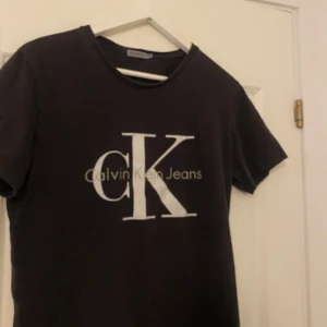 Svart t-shirt från Calvin Klein Jeans - Svart t-shirt från Calvin Klein Jeans med stor vit logga på bröstet. Klassisk rund halsringning och korta ärmar. Perfekt för en stilren och enkel look.