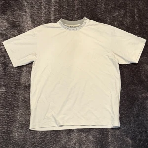 Vit t-shirt från Acne Studios - Vit t-shirt från Acne Studios med tryckt logga runt halsringningen. Klassisk passform och korta ärmar, perfekt för en clean och stilren look. Mjukt material som känns skönt mot huden. Använd ett fåtal gånger. Storlek s men passar även M