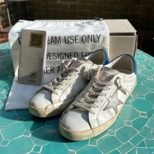 Vita sneakers från Golden Goose med blå detalj - Säljer ett par Golden Goose Super-Star i storlek 40. Allt på bilderna följer med vi köp! Kontakta gärna vi intresse! Priset går att diskutera vid snabb affär!
