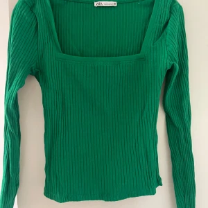 Grön  långärmad topp  - Säljer en snygg grön ribbstickad topp från Zara med fyrkantig ringning och långa ärmar. Perfekt att styla till jeans eller kjol för en trendig look. Toppens material är stretchigt och sitter skönt på kroppen. Knappt använd