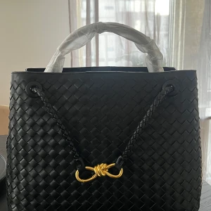 Bottega Veneta - Säljer en svart läder handväska i flätat skinn med guldfärgad metall-detalj framtill. Väskan har två handtag och en klassisk, elegant design som passar till många tillfällen. Alla logor är på rätt platser. Den är 32cm bred och 25cm hög så får plats med en laptop i och är användbar rymlig vardagsväska. Ej använd. Pris kan justeras vid snabb affär 🌸