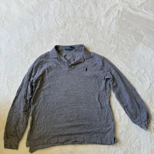 Grå långärmad pikétröja från Polo Ralph Lauren L - Säljer en klassisk grå långärmad pikétröja från Polo Ralph Lauren. Tröjan har krage, knäppning vid halsen och den ikoniska broderade loggan på bröstet. 