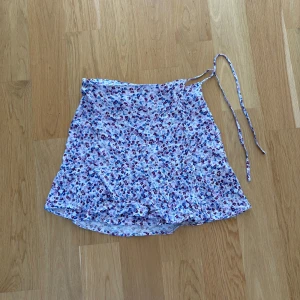 Kort blommig kjol - Kort kjol från Pull&Bear som man knyter samt knäpper med en knapp, bra skick 
