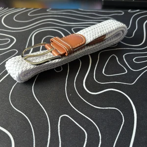 Vitt flätat bälte med bruna skinn-detaljer - Snyggt vitt flätat bälte med detaljer i brunt skinn och ett silvrigt spänne. Perfekt accessoar för att lyfta din outfit med en fräsch och stilren look. Passar till både jeans och chinos.