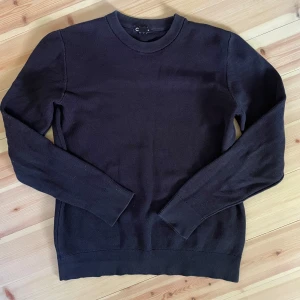 Mörkblå tröja - En stilren mörkblå stickad tröja från Cubus med rund halsringning och långa ärmar. Tröjan har en diskret struktur i materialet och ribbade muddar vid ärmslut och nederkant. 