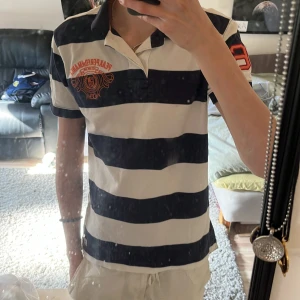 Pikétröja från Peak Performance - Säljer en klassisk och stilren pikétröja från Peak Performance i marinblått och vitt med breda ränder. Tröjan har broderad logga på bröstet och siffran 86 i rött på ärmen. Skön bomullskvalitet och krage med knappar. Tveka inye på att höra av dig och priset är inte hugget i sten