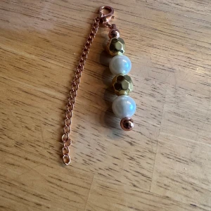Smycke  med pärlor och kedja - Snyggt smycke med roséguldfärgad kedja och pärlor i vitt och guld. Pärlorna är blandade med skimrande vita och guldmönstrade kulor. Perfekt accessoar för att lyfta din outfit.