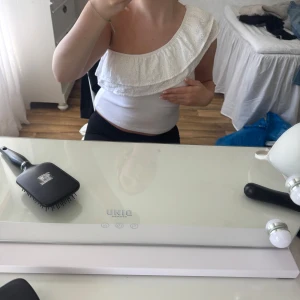 Vit one shoulder topp med volang från Gina Tricot - Säljer en vit one shoulder topp från Gina Tricot med bred volangdetalj över axeln. tillverkad i ett mjukt bomullsmaterial. Perfekt för sommarens varma dagar!