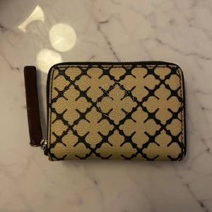 Beige och svart plånbok från Marlene Birger  - Säljer en beige plånbok från Marlene Birger  med klassiskt svart mönster och dragkedja runtom. Perfekt storlek för kort och kontanter.