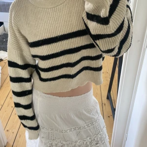 Beige och svart randig croppad stickad tröja - Säljer en croppad stickad tröja i beige med svarta ränder. Tröjan har lång ärm, rund halsringning och är oversized i modellen. Perfekt för lager-på-lager och chill dagar.