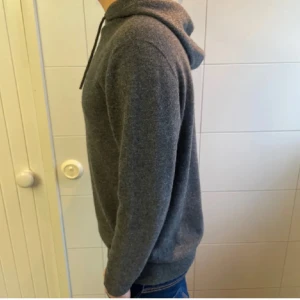 Grå merinoull hoodie - Säljer en enkel och stilren grå hoodie med huva och dragsnören. Den är gjord i merinoull som ser ut som kashmir men både håller bättre och är billigare. Passar riktigt bra med ett par jeans, tröjan är knappt andvänd och har skick 10/10