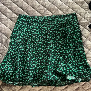 Svart och grön blommig kjol från Zara - Snygg svart kjol med grönt blommönster från Zara. Kjolen har en kort längd och en bekväm passform, perfekt för en trendig look. Tillverkad i ett lätt och luftigt material.