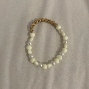 Armband med pärlor och stjärnor - Charmigt armband med vita pärlor och guldfärgade stjärnor. Perfekt för att lägga till en touch av elegans till din outfit. Armbandet har en elastisk design för enkel användning.