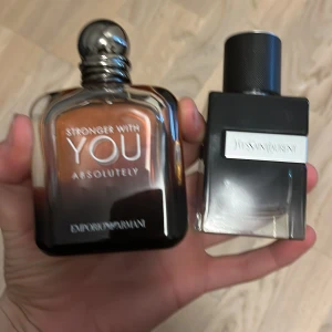 Parfymer från Emporio Armani och YSL - Två exklusiva parfymer: 'Stronger With You Absolutely' från Emporio Armani med en elegant brun flaska och metallkork, samt en stilren svart flaska från YSL med en silveretikett. Perfekta för den som vill ha en sofistikerad doft.