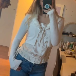 Vit ribbad bolerotopp med knyt - Säljer en söt vit ribbad bolerotopp med knyt framtill och en fluffig krage. Toppen har långa ärmar och en croppad passform, perfekt för att lägga till en extra touch till din outfit.