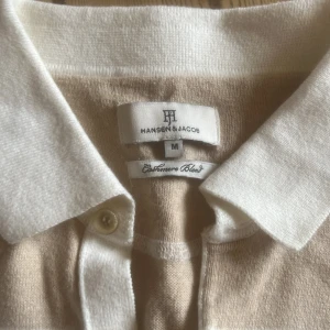 Randig pikétröja från Hansen & Jacob - Säljer en stilren randig pikétröja från Hansen & Jacob i beige och vit. Tröjan är tillverkad i en mjuk cashmere-blandning och har långa ärmar samt en klassisk krage med knappar. Perfekt för en avslappnad men ändå elegant look. Perfekta färgkombinationer inför sommaren. Tröjan är storlek m men kan också passa s. Priset går att diskutera vid snabb affär. Nypris var 1800 kr, mitt pris 749 kr.