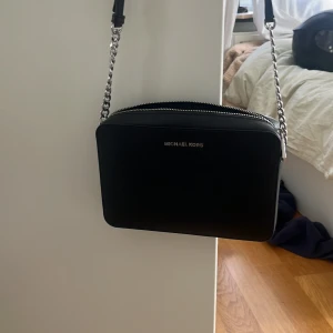 Svart axelväska från Michael Kors - Snygg svart axelväska från Michael Kors med silverfärgade kedjedetaljer. Köpt för ett halv år sen för 2200kr. Väskan är i helt nytt skick och väldigt snygg. Pris kan diskuteras.