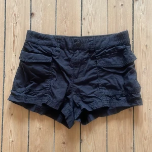 Svarta shorts från H&M Divided - Säljer ett par svarta shorts från H&M Divided. De har praktiska fickor och en knapp framtill. Perfekta för en avslappnad stil.
