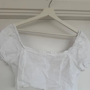 Vit kortärmad blus - Säljer en söt vit blus med korta puffärmar och elastisk smockdetalj i ryggen. Perfekt för sommardagar och går även att ha som off-shoulder. Cropped design 