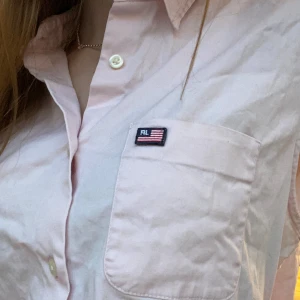 Ljusrosa ärmlös skjorta från Ralph Lauren - Säljer en stilren ljusrosa ärmlös skjorta från Ralph Lauren. Skjortan har en klassisk krage och knappar framtill. Funkar som fintröja men också att ha till vardags, jag har xs och på mig sitter den som på bilderna för referens