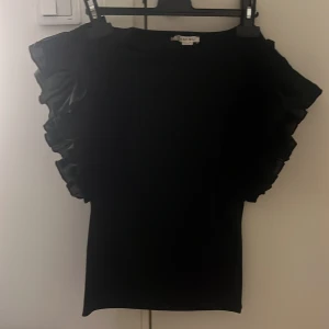 Vit och svart topp med volangärmar från Amisu - Säljer en stilren vit och svart topp från Amisu med volangdetaljer på ärmarna. Perfekt för att ge en extra touch till din outfit. Toppen har en normal passform och är tillverkad i ett mjukt material. Helt nya utan prislapp. Storlek M men passar mig som har Xs i tröjor 200 för båda 120kr/st