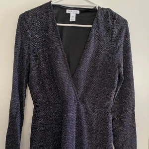 Svart glittrig klänning från NLY One - Snygg svart klänning från NLY One med glittrande detaljer. Den har en v-ringad design och långa ärmar, perfekt för en kväll ute. Klänningen är i en bekväm passform och ger en elegant look.