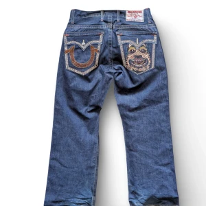 Supersällsynta True Religion Jeans - Mörkblå True Religion-jeans med rhinestones på alla fickor. Det här paret är riktigt unikt – det finns just nu bara ett enda exemplar i världen, och det är jag som håller i dem. Men jag vill bli av med dem eftersom jag behöver pengarna.  Storlek: Ca 34 (EU 50) baserat på midjemåttet Skick: Jeansen är i bra skick överlag, men några av stenarna på vänster bakficka har trillat av. Som tur är har jag kvar dem, så det är bara at
