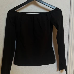 Svart offshoulder topp - Snygg svart offshoulder topp med långa ärmar och en stilren design. Perfekt för en trendig look. Toppen har en elastisk kant för en bekväm passform.