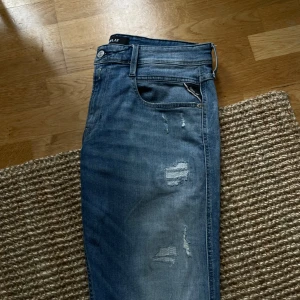 Blå jeans från Replay - Snygga blå jeans från Replay med slitna detaljer och en klassisk femficksdesign. De har en knappgylf och bälteshällor, vilket ger en tidlös look. Perfekta för en avslappnad stil. W33 men skulle säga att dom sitter som 31