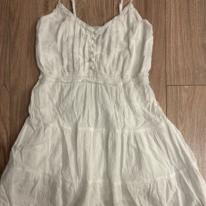 Vit klänning från NLY Blush - Säljer en söt vit klänning från NLY Blush med smala axelband och knappar framtill. Klänningen har en lätt och luftig design, perfekt för varma dagar. Den har en fin struktur och en feminin siluett som ger en romantisk känsla. Perfekt för sommarens alla tillfällen! 🌸pris kan dirkuteras💞