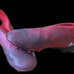 Röda fotbollsskor från Adidas - Snygga röda fotbollsskor från Adidas med en strömlinjeformad design och mönstrad yta. Skorna har en låg profil och är perfekta för snabba rörelser på planen. De har en elastisk öppning för enkel påtagning.