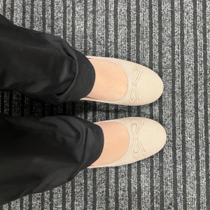 Beige ballerinaskor med rosett - Säljer ett par eleganta beige ballerinaskor med en söt rosett på ovansidan. Skorna har en rund tå och är tillverkade i ett syntetmaterial med en lätt textur. Perfekta för en stilren look. Säljer pga att dom är för stora för mig. 