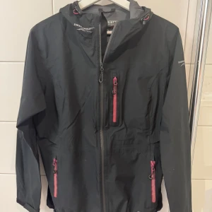 Svart vind- och regnställ från Swedemount - Säljer ett svart vind-/regnställ från Swedemount. Jackan och byxorna har rosa detaljer på dragkedjorna och är perfekta för blåsiga dagar och lagomt regniga dagar. Jackan är i storlek 38 och byxorna i storlek 36.