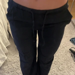 Svarta linnebyxor från Gina Young  - Säljer ett par svarta byxor från Gina Tricot med snörning i midjan. Perfekta för en avslappnad stil och bekväma att bära. Passar bra till olika tillfällen och kan enkelt matchas med olika toppar.