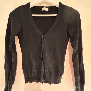 Svart kofta från Vero Moda - Säljer en stilren svart kofta från Vero Moda. Koftan har en v-ringad design med knappar framtill och långa ärmar. Perfekt för lager-på-lager-stil eller som ett enkelt tillskott till din garderob. Kontakta mig om det är något. Köparen står för frakten💗
