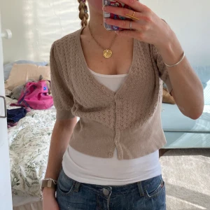 trekvartsärm kofta med knappar - Säljer en beige kofta med trekvarts ärmar och knappar framtill. Koftan har ett diskret mönster och är croppad, vilket ger en trendig look. Perfekt för lager-på-lager-stil. Storlek s💓💓