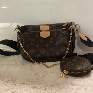 Brun axelväska med monogram - Snygg brun axelväska med klassiskt monogrammönster och guldkedja. Väskan har flera fack och en avtagbar liten rund plånbok. Perfekt för att hålla ordning på dina saker med stil.