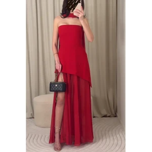 Röd axelbandslös långklänning - Elegant röd axelbandslös långklänning med asymmetrisk design och transparent nederdel. Perfekt för en glamorös kväll. Klänningen har en slits och ett flytande tyg som ger en dramatisk effekt. nypris 4200